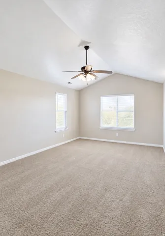 Vaulted ceiling with a ceiling fan, dual windows with blinds, and neutral carpeting