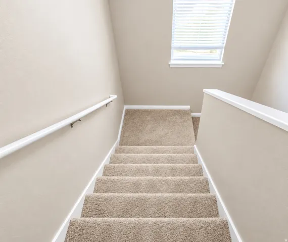 Carpeted staircase with a window featuring blinds and a white handrail