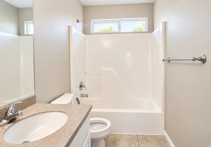 White tub and shower combination with chrome fixtures, a toilet, a vanity with an integrated sink and countertop, and a window for natural light