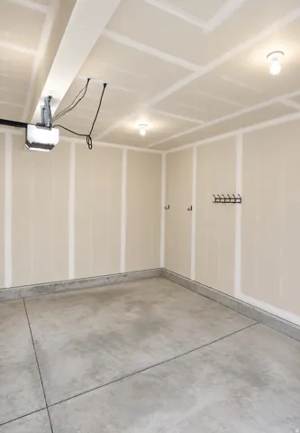 Concrete flooring, finished drywall walls, overhead lighting, and an installed garage door opener