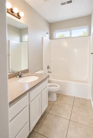 Guest bathroom with full vanity with integrated sink and stone-finish countertop, tiled flooring, white bathtub with shower, and transom windows