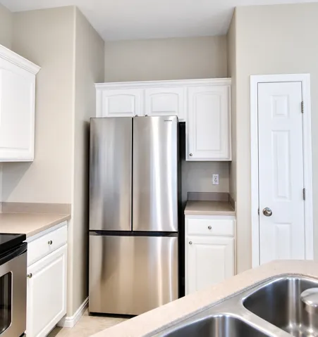 Stainless steel French door refrigerator, white upper and lower cabinetry, light-toned countertops, and a double basin stainless steel sink