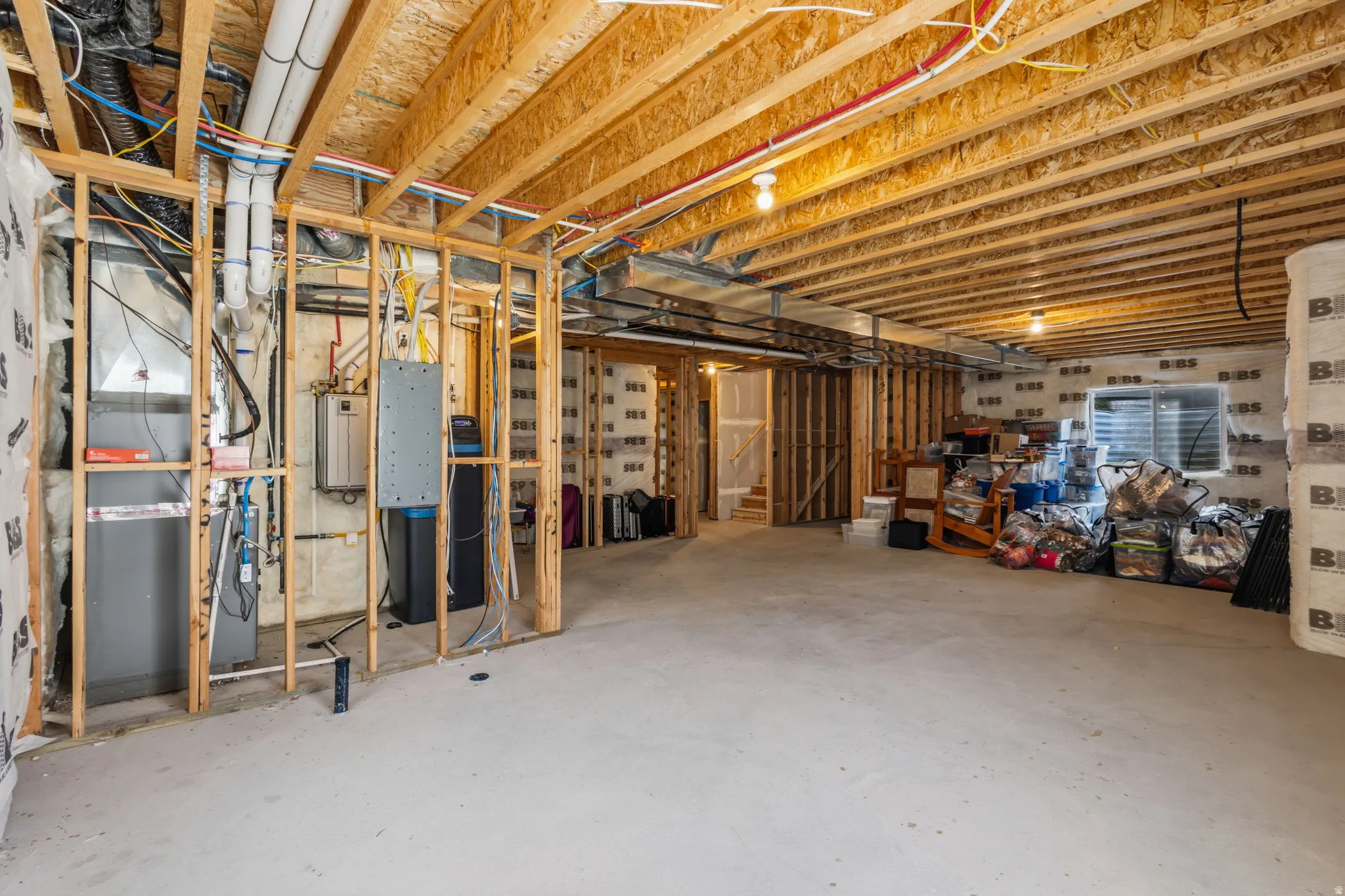 Unfinished basement with exposed wood framing, concrete flooring, rough plumbing, and visible utility systems