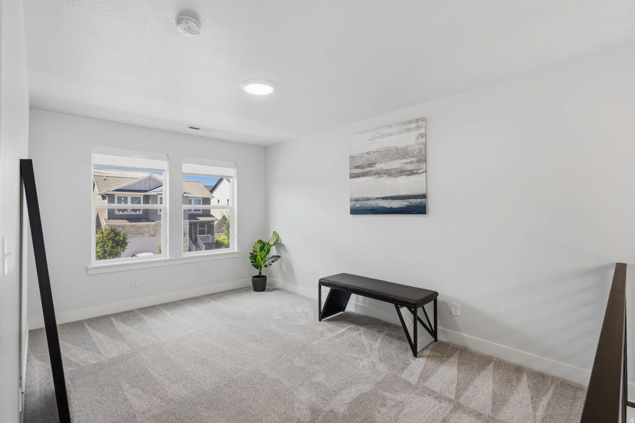Recessed lighting, large windows, light grey carpet, white walls, and a dark-toned railing