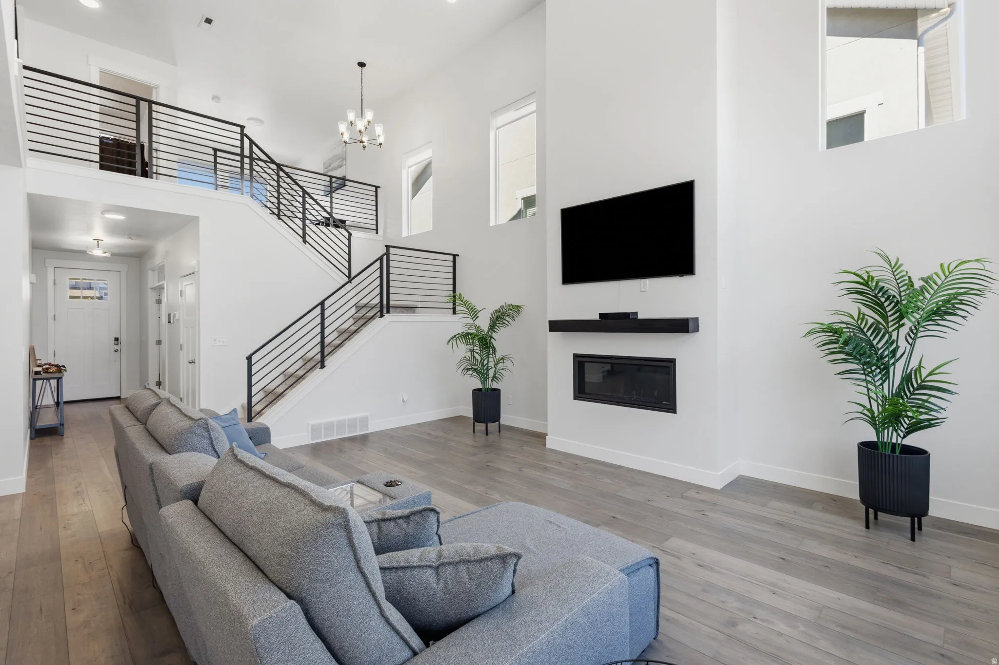 Open concept living area featuring a prominent staircase with black horizontal railings, high ceilings, wood-finish flooring, and an integrated fireplace with a built-in media shelf