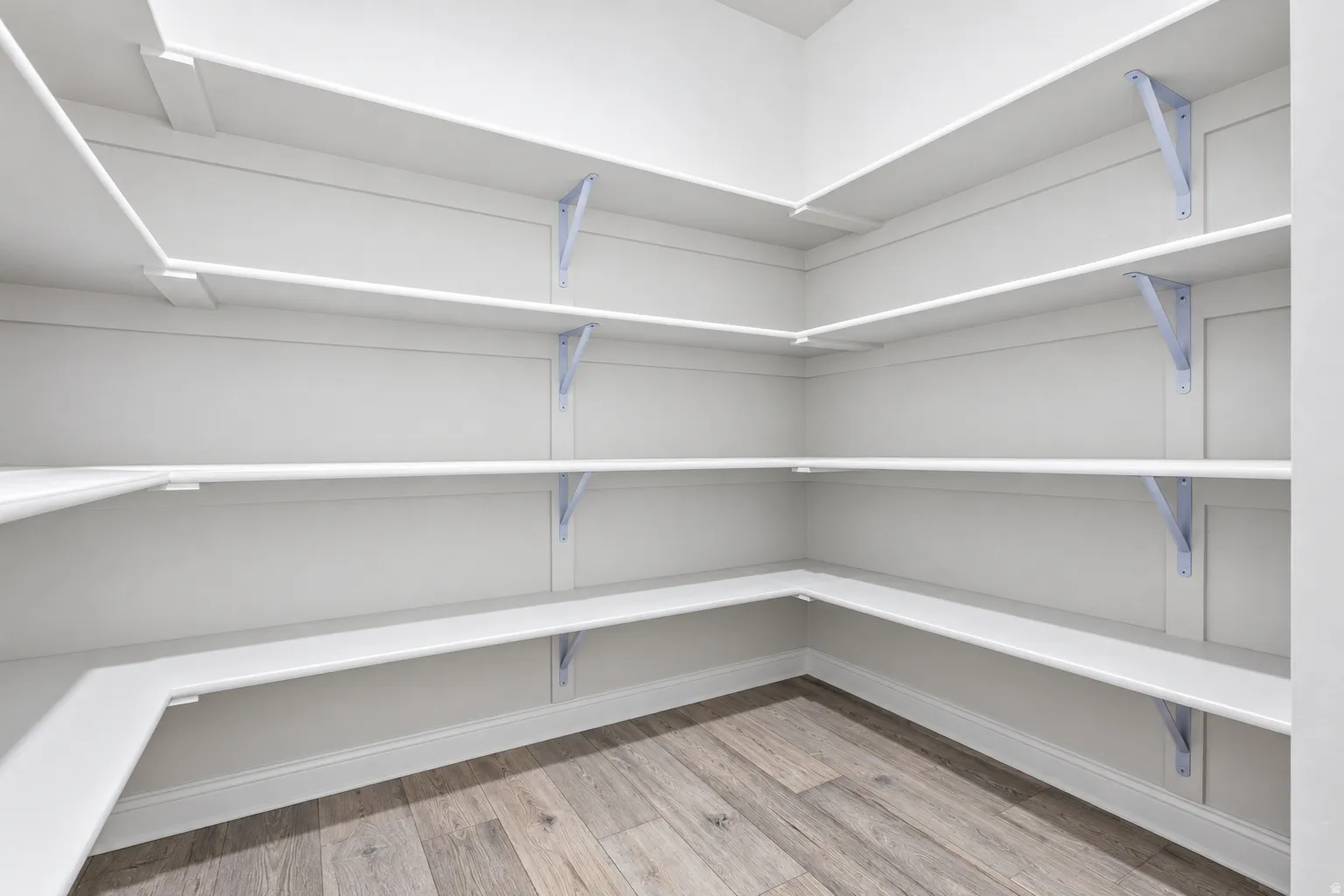 Walk-in pantry featuring white shelving, light wood-finish flooring, and white baseboards