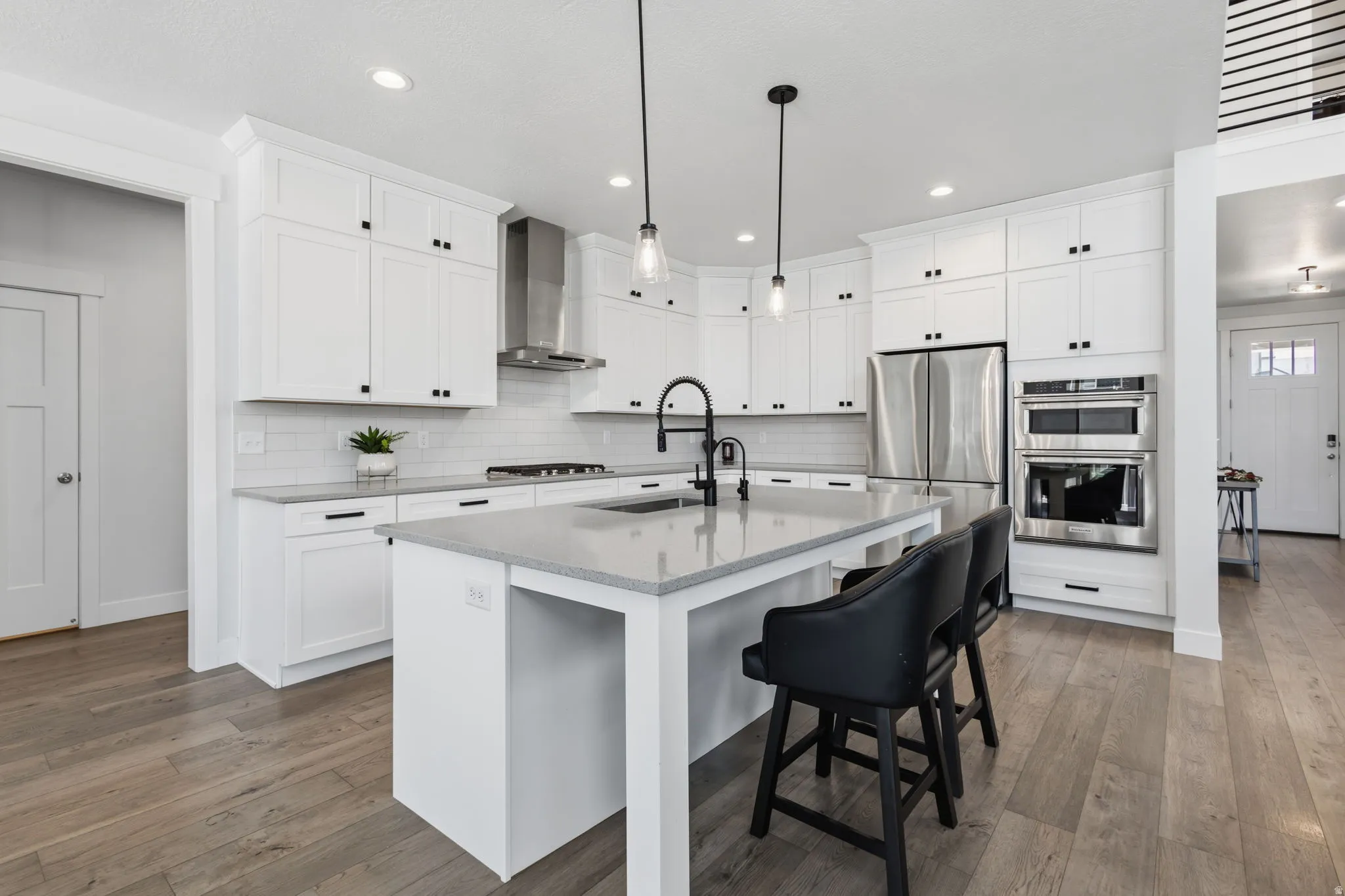 Kitchen featuring white shaker-style cabinetry, stainless steel appliances, a center island with countertop seating, light-colored countertops, and wood-finish flooring