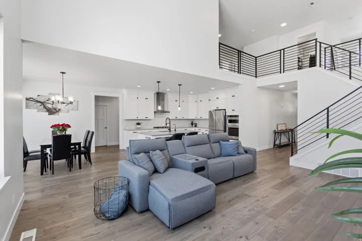 Open-concept living space featuring wood-finish flooring, a two-story ceiling, a contemporary kitchen with white cabinetry, and a staircase with sleek horizontal railings