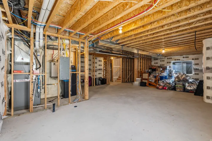 Unfinished basement with exposed wood framing, concrete flooring, rough plumbing, and visible utility systems
