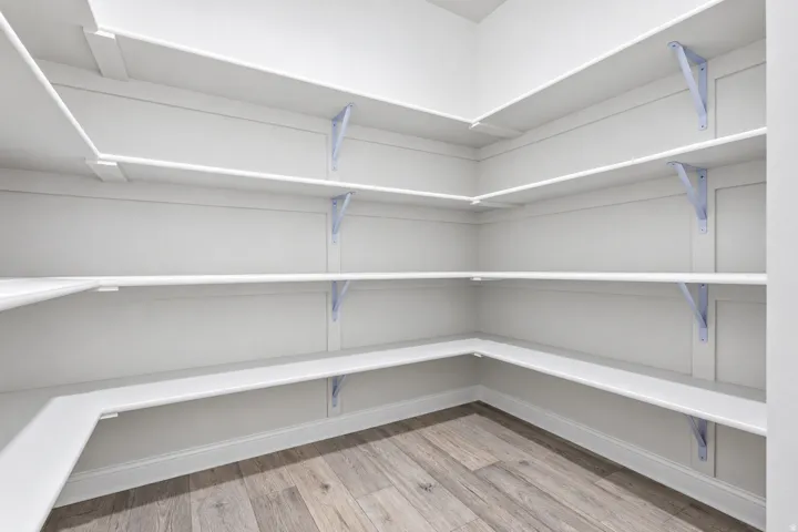 Walk-in pantry featuring white shelving, light wood-finish flooring, and white baseboards