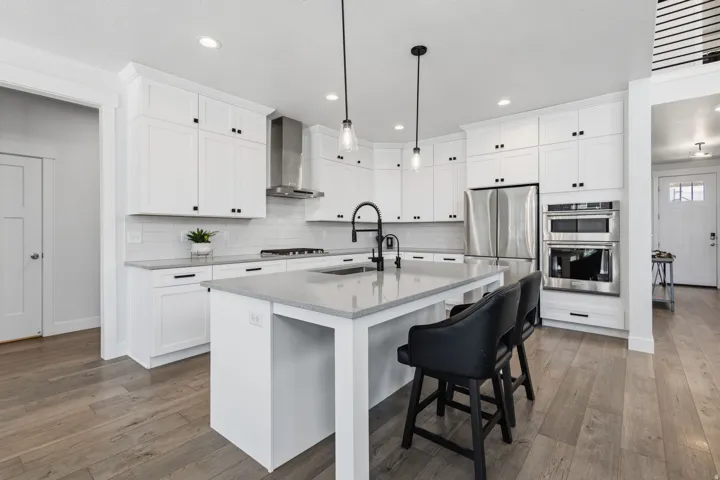 Kitchen featuring white shaker-style cabinetry, stainless steel appliances, a center island with countertop seating, light-colored countertops, and wood-finish flooring