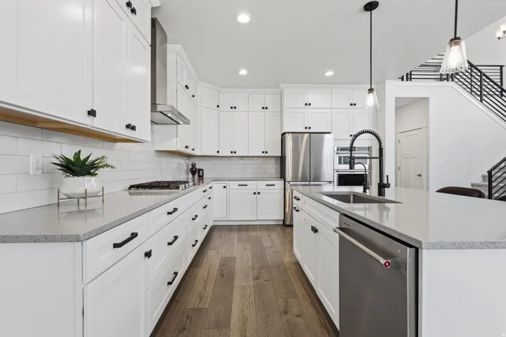 White cabinetry with matte black hardware, stainless steel appliances, wood-finish flooring, light-toned countertops, and a subway tile backsplash