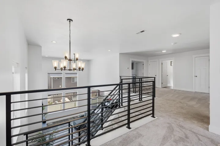 Loft area with contemporary black metal railings, recessed lighting, and a multi-light chandelier