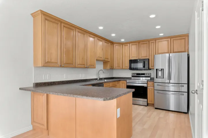 Kitchen featuring wood-finish cabinetry, dark countertops, white subway tile backsplash, and stainless steel appliances