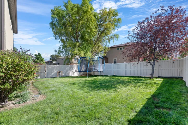 Fenced backyard featuring a manicured lawn, mature trees, and established shrubbery