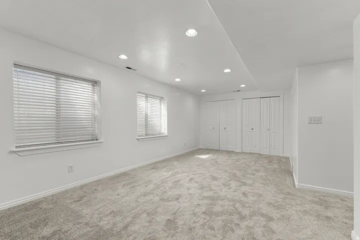 Recessed lighting, two windows with blinds, light gray carpet, and two sets of bi-fold closet doors