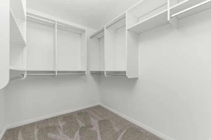 White built-in shelving, multiple hanging rods, corner shelving unit, and gray carpet flooring