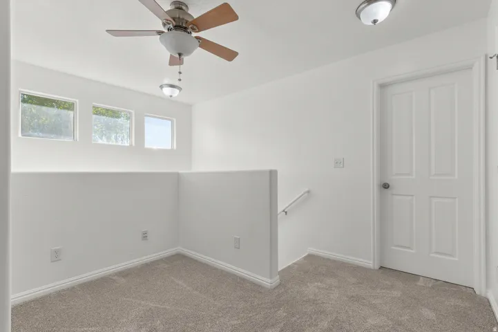 Carpeted loft area with a ceiling fan, three horizontal windows, and a panel door