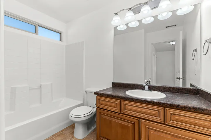 White tub and shower combination with tile-look surround, wood-finish vanity with an integrated sink, dark countertop, and large wall-mounted mirror