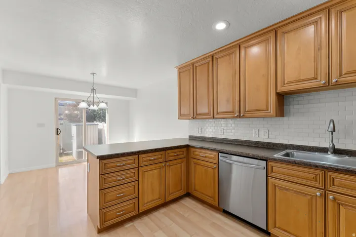 Wood-finish flooring, wood cabinetry with ample storage, stainless steel dishwasher, integrated sink, and white subway tile backsplash