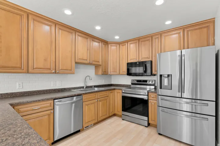 Kitchen featuring wood cabinetry, stainless steel appliances, white subway tile backsplash, recessed lighting, and wood-finish flooring