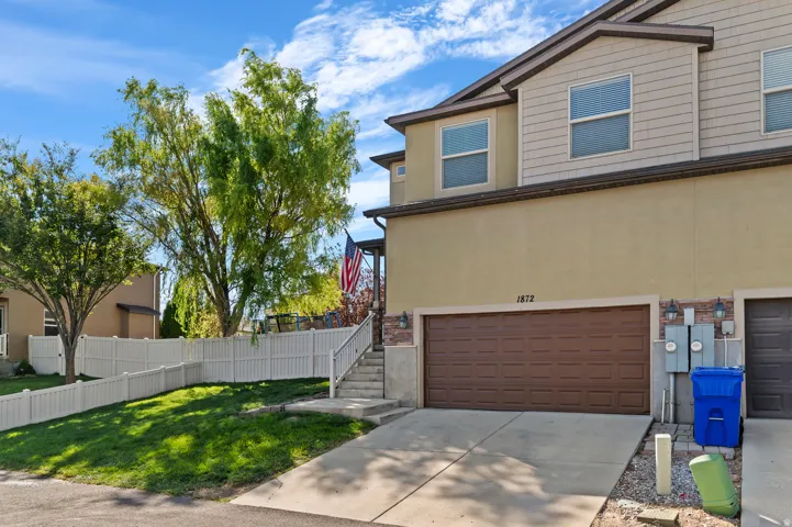 Stucco and siding exterior with a brown panel garage door, concrete driveway, and a white fence enclosing a sloped lawn