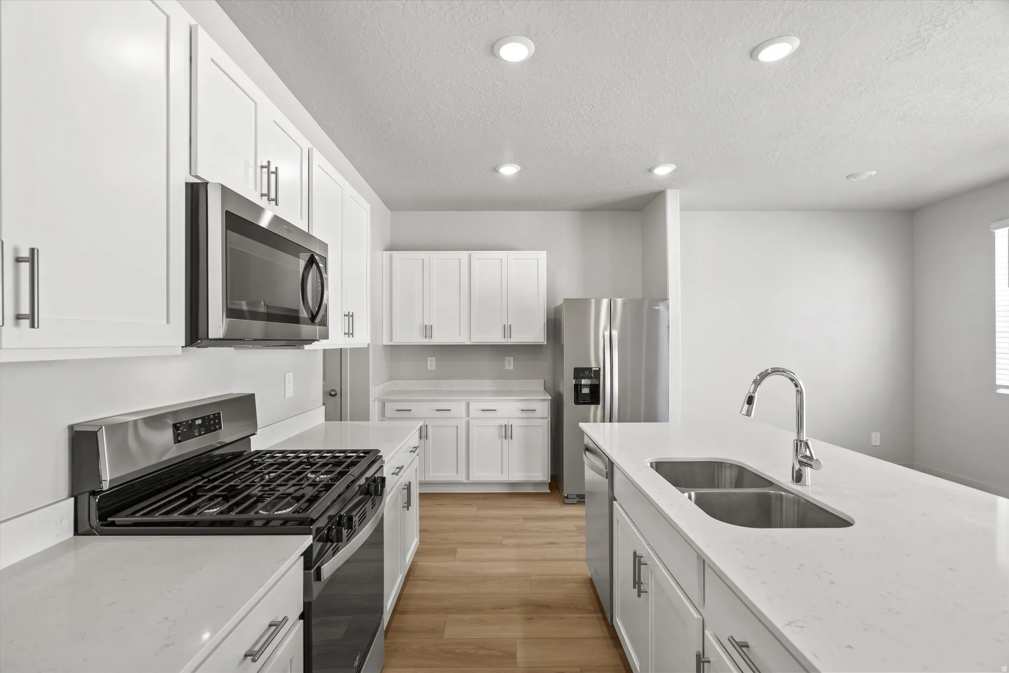 White cabinetry, stainless steel appliances, wood-finish flooring, recessed lighting, and a kitchen island with an undermount double-basin sink