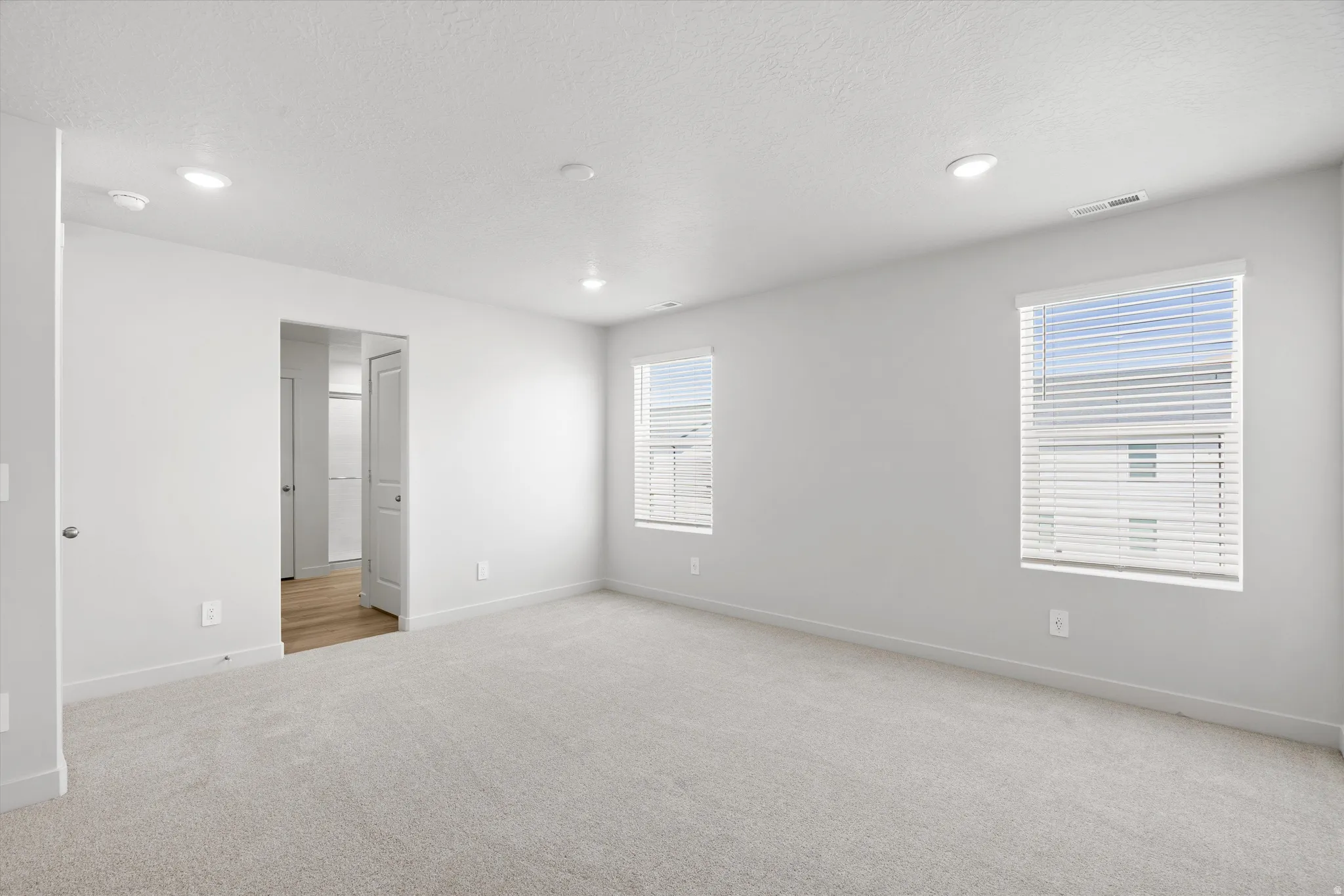 Spacious room featuring carpeting, two windows with blinds, recessed lighting, and white walls