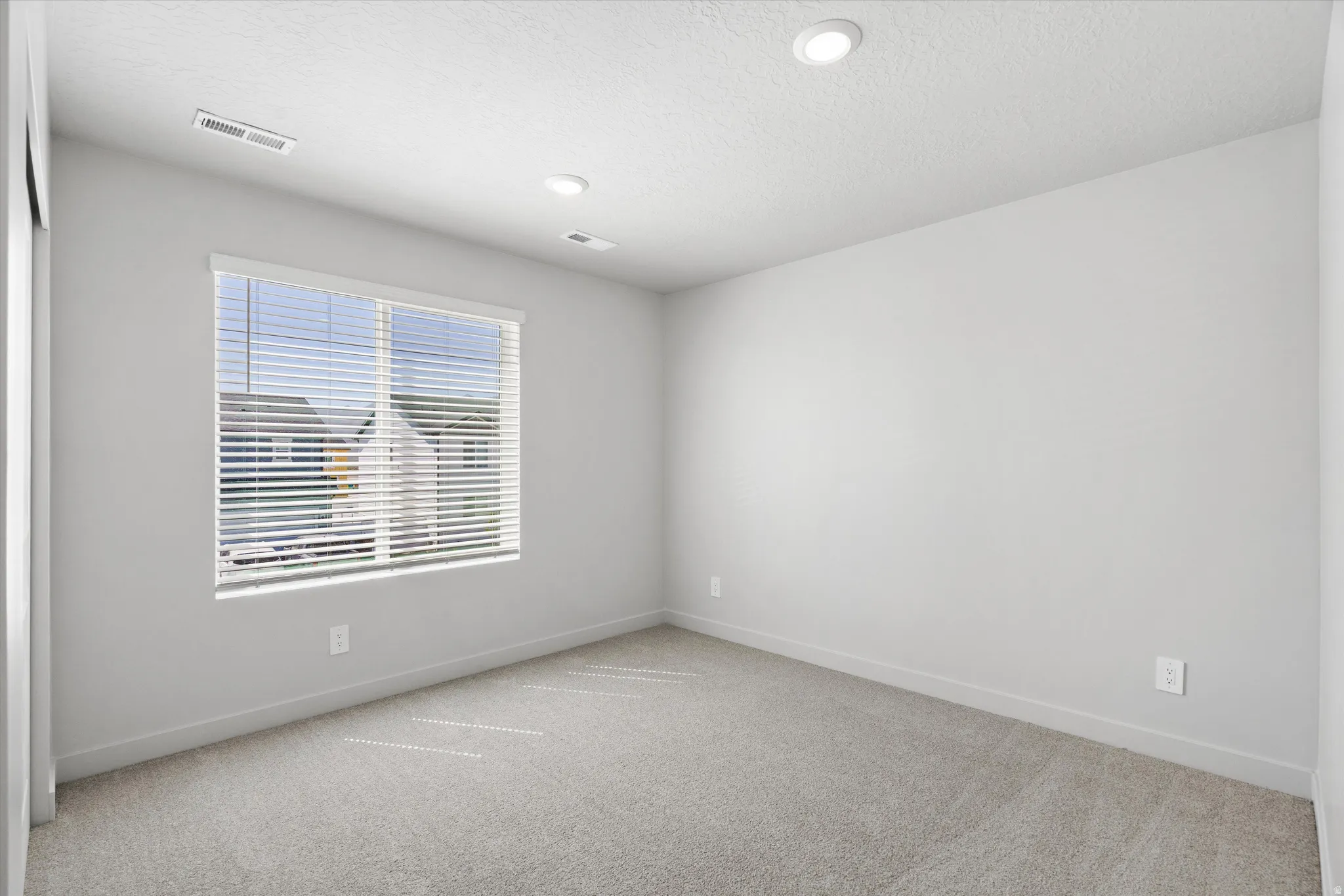 Recessed ceiling lighting, light gray wall finish, window with blinds, light gray carpeting, and white trim