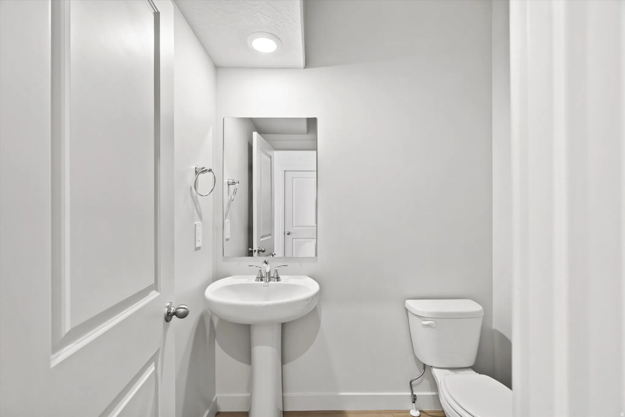 Pedestal sink with chrome faucet, wall-mounted mirror, and recessed lighting