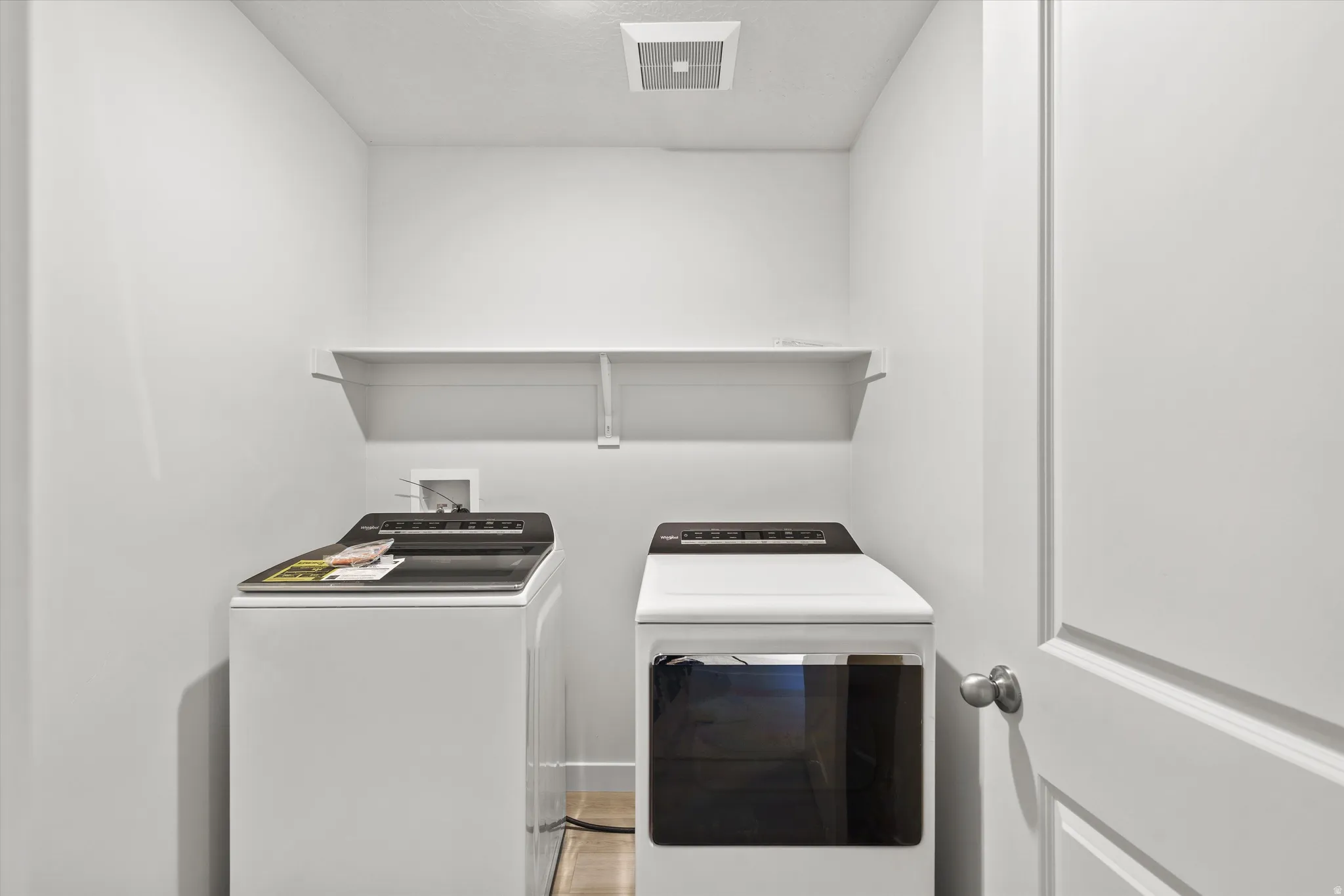 Compact utility space featuring a wall-mounted shelf, light-toned flooring, and a panel-style door