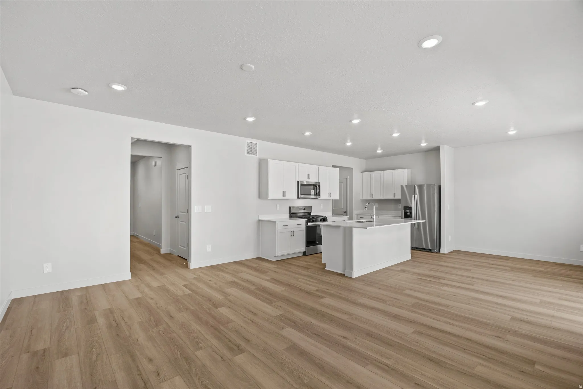 Wood-finish flooring throughout, recessed lighting, and a kitchen featuring white cabinetry, a kitchen island, and stainless steel appliances