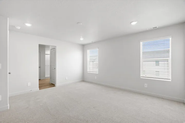 Spacious room featuring carpeting, two windows with blinds, recessed lighting, and white walls