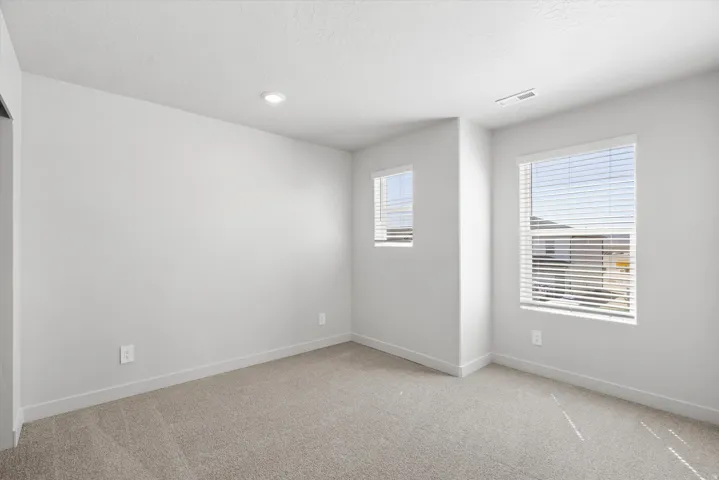 Neutral-toned carpeting, recessed ceiling lighting, and multiple windows with blinds