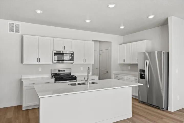 Kitchen featuring white shaker cabinetry, stainless steel appliances, light-toned countertops, a central island with an integrated sink, and wood-finish flooring
