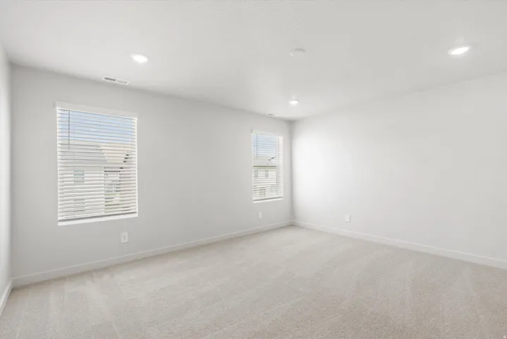 Recessed lighting, light-toned carpeting, two windows with blinds, and neutral wall paint
