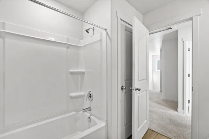 White tub and shower combination with chrome fixtures and integrated shelving