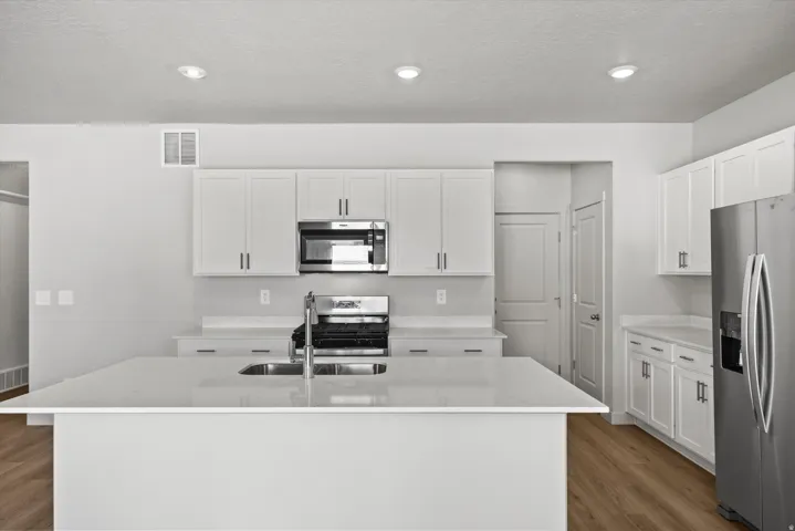 Kitchen featuring white cabinetry, stainless steel appliances, light-toned countertops, a kitchen island with an undermount sink, and wood-finish flooring