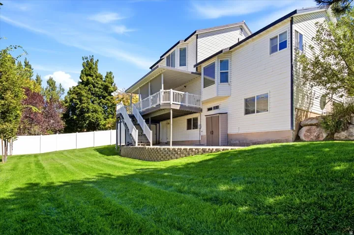 Expansive lawn with a white privacy fence, multi-level deck with white railings, and a lower-level patio with a retaining wall
