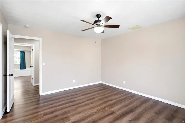 Expansive room featuring wood-finish flooring, light neutral walls, and a ceiling fan with integrated lighting