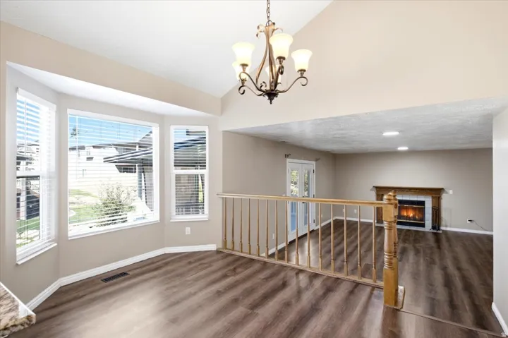 Bay window with multiple panels, wood-finish flooring, vaulted ceiling, decorative chandelier, and fireplace with wood mantel