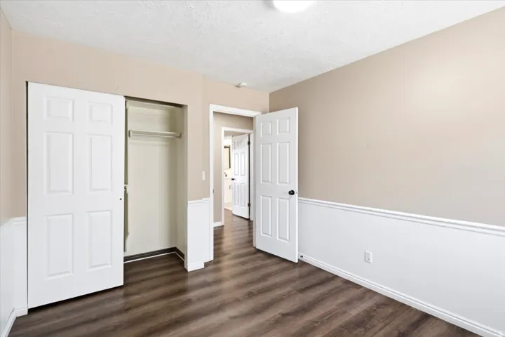 Wood-finish flooring, half-wall wainscoting, neutral wall paint, ceiling-mounted light fixture, and a built-in closet with sliding doors