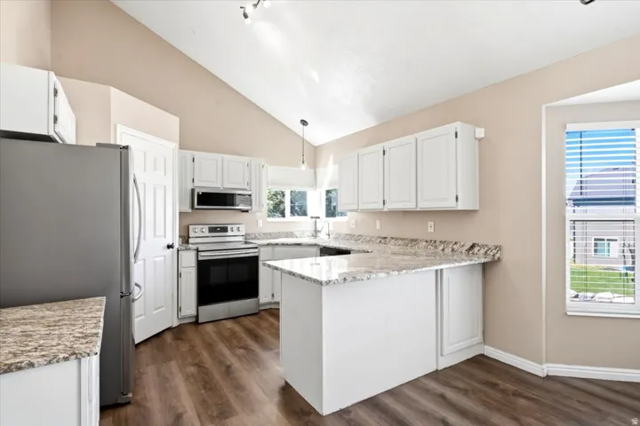Kitchen featuring white cabinetry, stainless steel appliances, wood-finish flooring, vaulted ceiling, and a peninsula with a stone-finish countertop