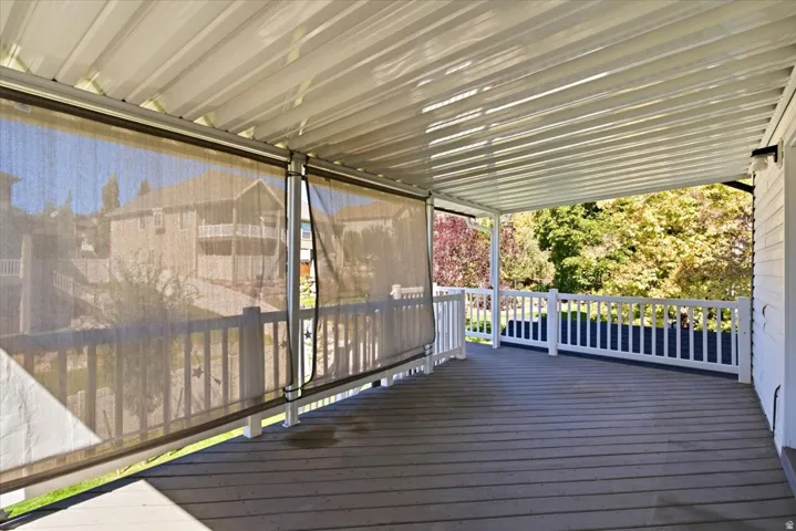 Covered deck featuring a white railing, wood-finish flooring, and retractable privacy screens