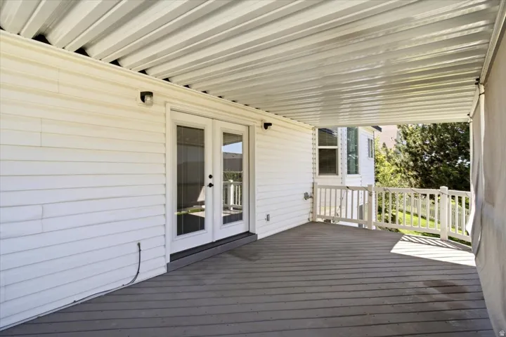 Covered outdoor deck with white siding, white French doors, a white railing, and a corrugated metal ceiling