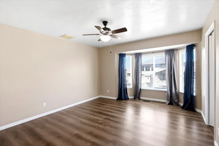 Bay window with blinds, wood-finish flooring, ceiling fan with integrated lighting, and neutral wall tones
