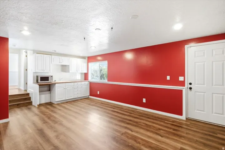 Wood-finish flooring, white cabinetry, light-colored countertops, interior door with matte black hardware, and a window with blinds