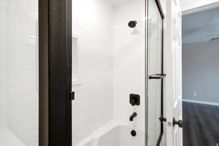 Bathtub with subway tile surround, matte black fixtures, and a clear glass shower enclosure