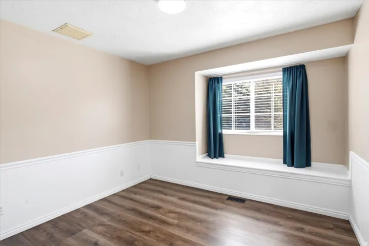 Wood-finish flooring, white wainscoting, recessed window with a built-in bench, and a flush-mount ceiling light