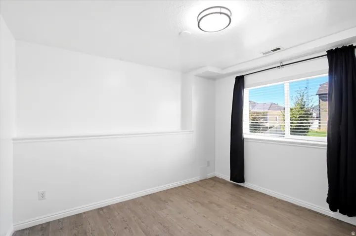 Neutral wall paint, wood-finish flooring, white window blinds, and a flush mount ceiling light fixture